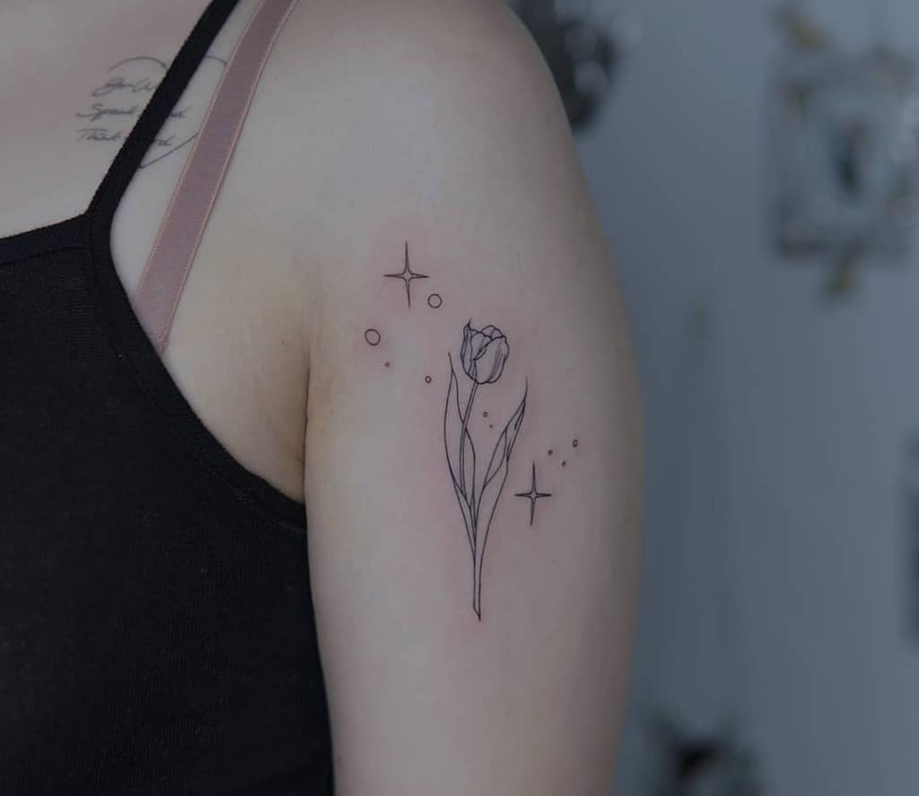 A minimalist tulip tattoo on the upper arm, featuring clean lines, a delicate flower, and whimsical sparkles and dots for a soft, ethereal touch.
