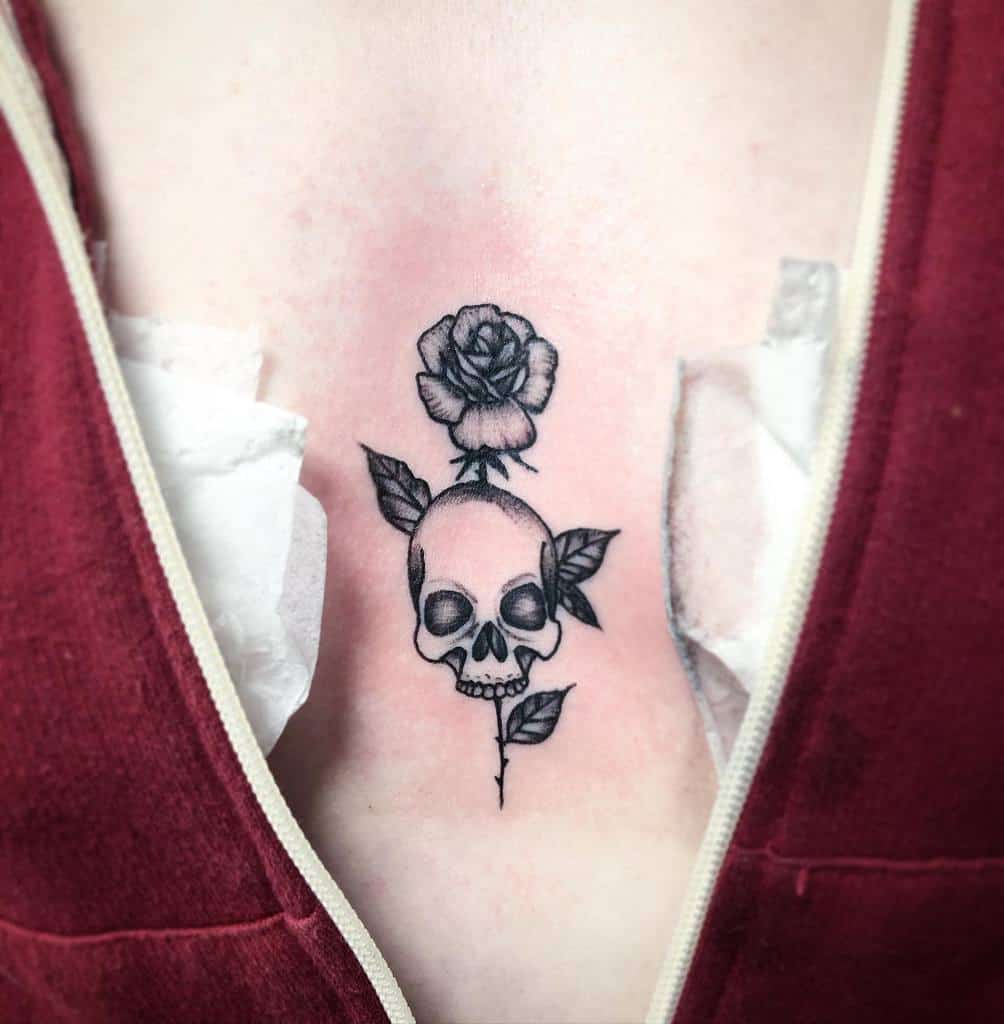 Minimalist black ink chest tattoo of a small skull with a blooming rose, symbolizing life and death with delicate linework.