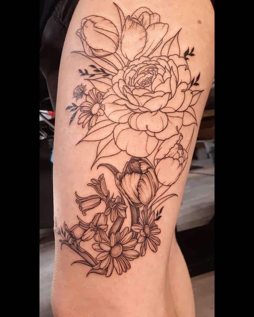 A detailed floral tattoo on the arm, featuring tulips, peonies, and daisies arranged in an intricate design with clean lines and shading.