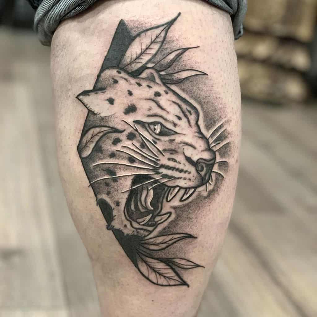 A bold black and grey tattoo of a snarling jaguar emerging from a geometric frame, surrounded by leaves, placed on the calf for a fierce look.