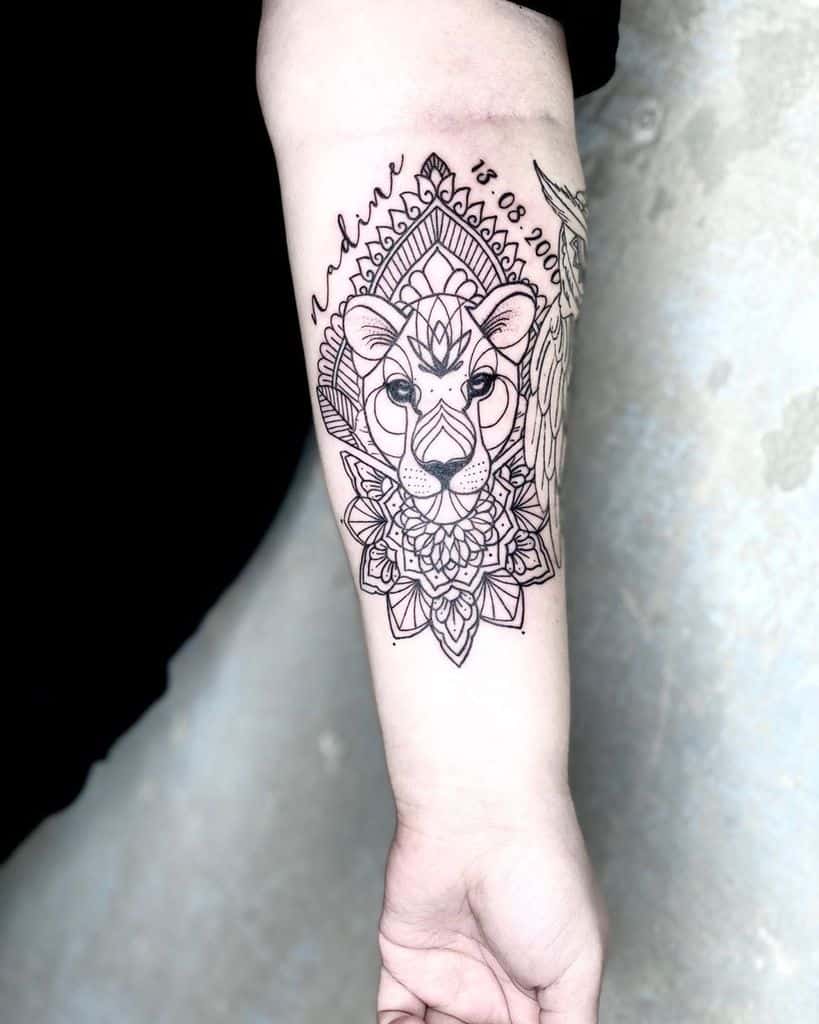 Intricate black linework lioness tattoo on the forearm, featuring mandala patterns, geometric elements, and a script date for a meaningful design.