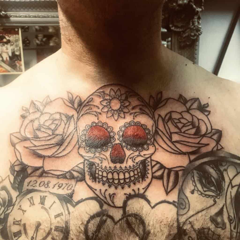 Chest tattoo featuring a colorful sugar skull with red accents, surrounded by roses, a clock, and intricate black ink details."