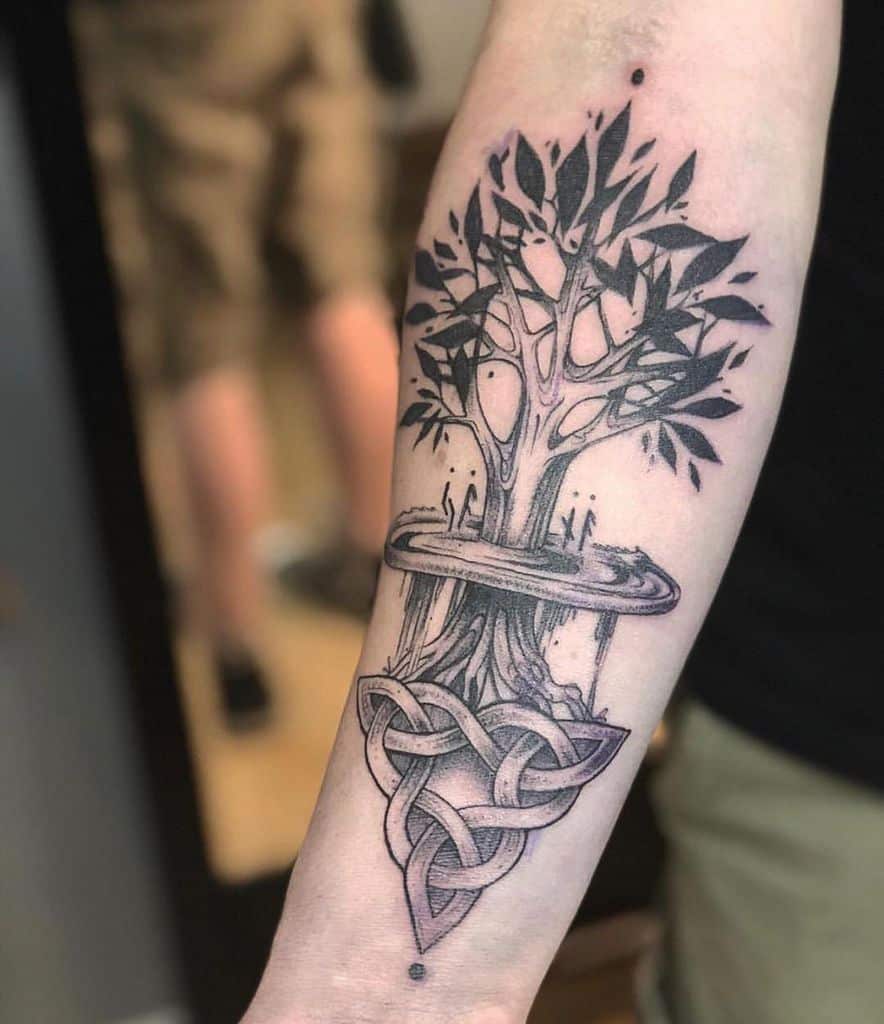 The tattoo features Yggdrasil with detailed roots intertwining into a Celtic knot, symbolizing connection, life, and Norse mythology.