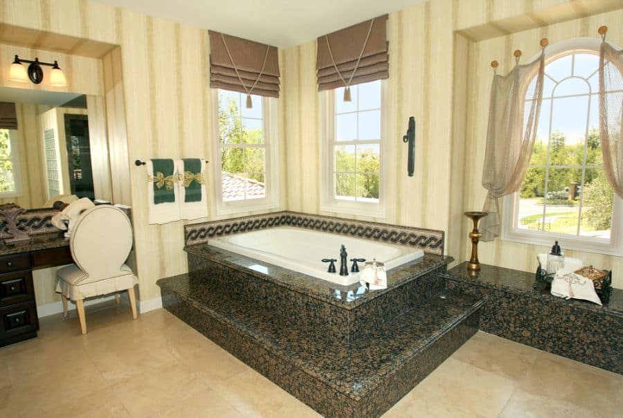 Luxurious bathroom with marble step-up tub, striped wallpaper, and arched windows with drapery.