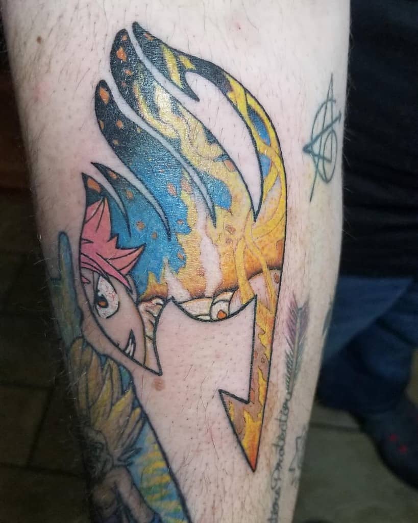 Vibrant Fairy Tail tattoo featuring the guild emblem with a fiery, cosmic design, revealing Natsu Dragneel’s intense gaze underneath.