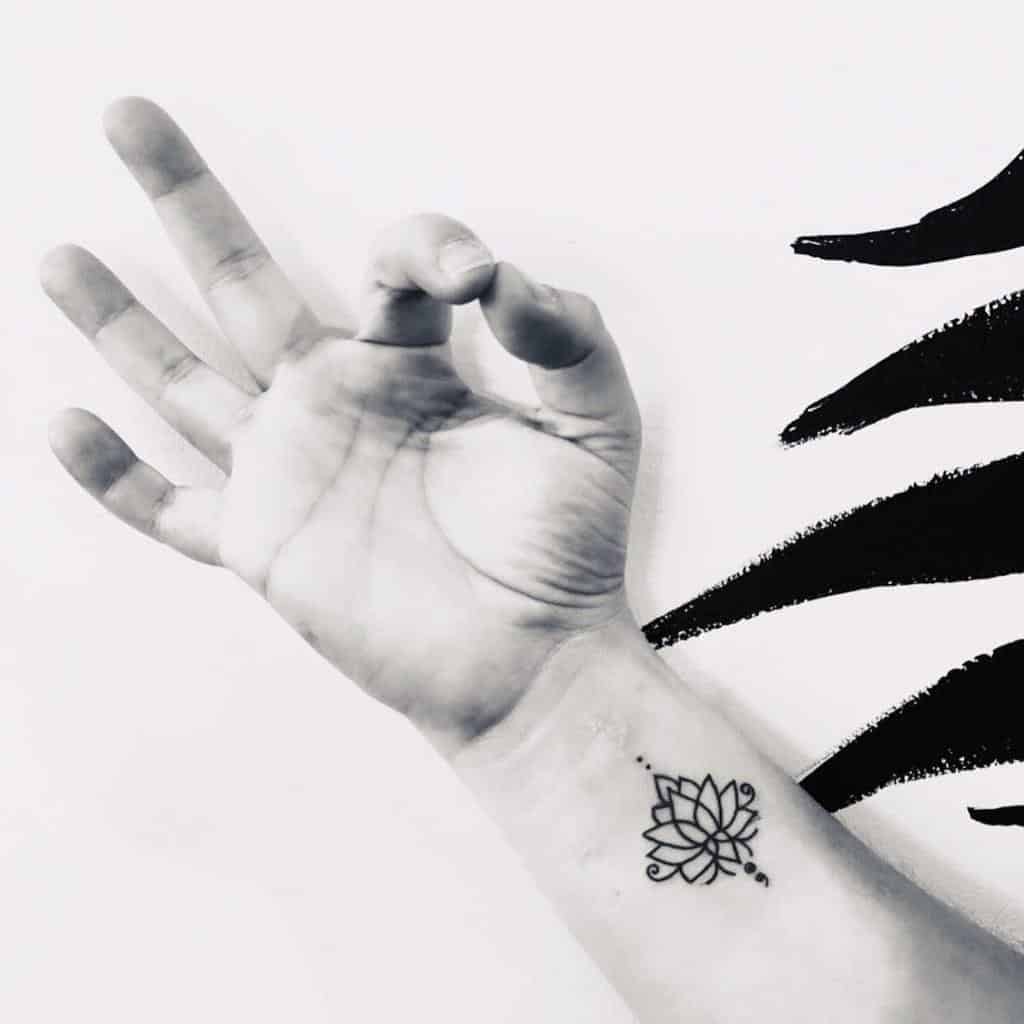 This tattoo combines a delicate lotus flower with a semicolon, symbolizing both personal growth and perseverance through life's challenges. The placement on the wrist is subtle yet meaningful.
