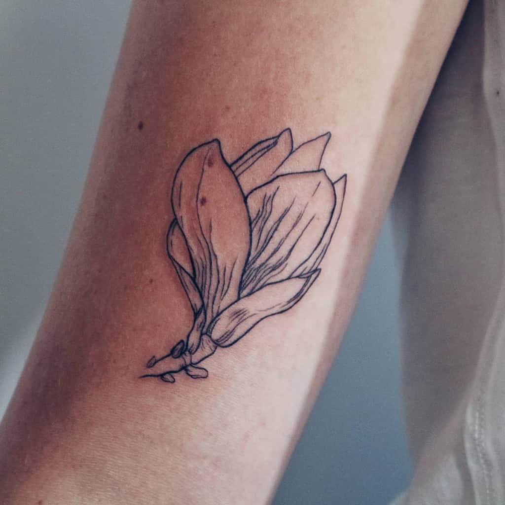 A line art tattoo of a magnolia graces the person's arm, adding a touch of elegance