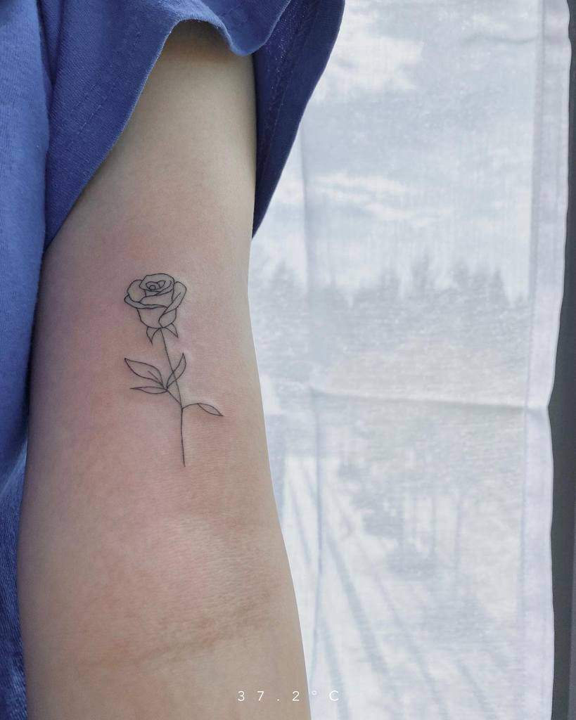 An arm adorned with a minimalist rose tattoo, its delicate stem artfully etched