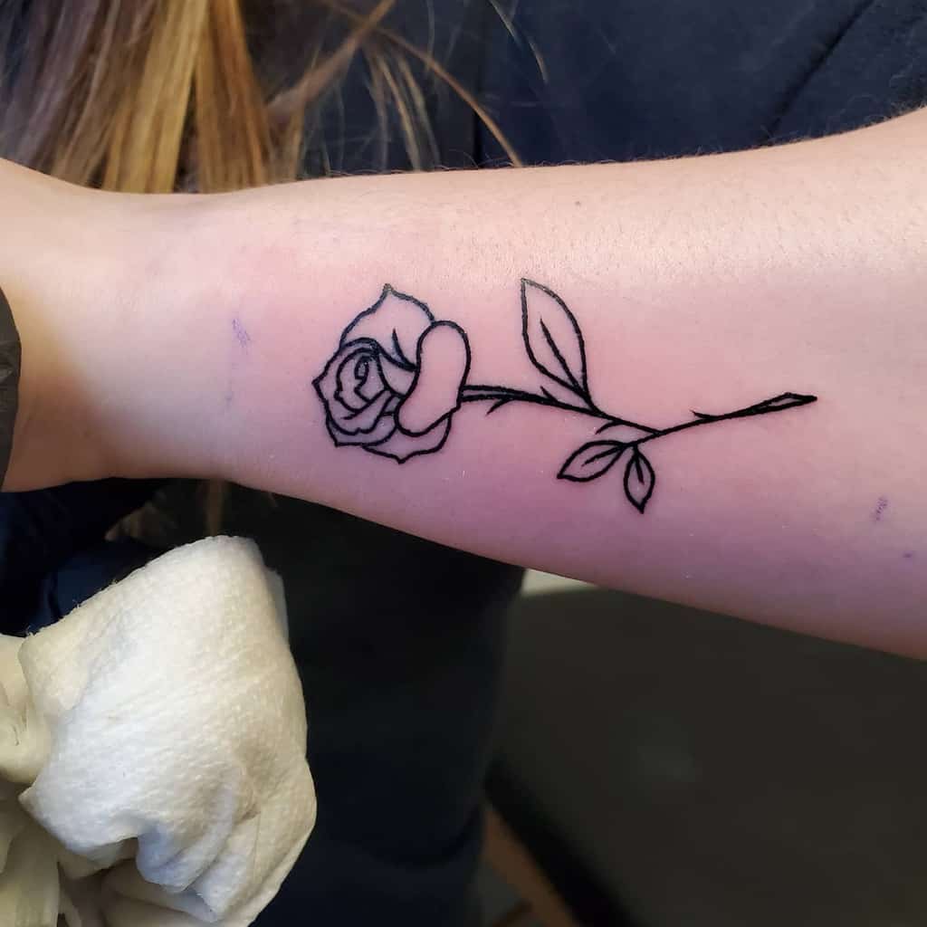Outline tattoo of a rose with a stem and leaves on a forearm