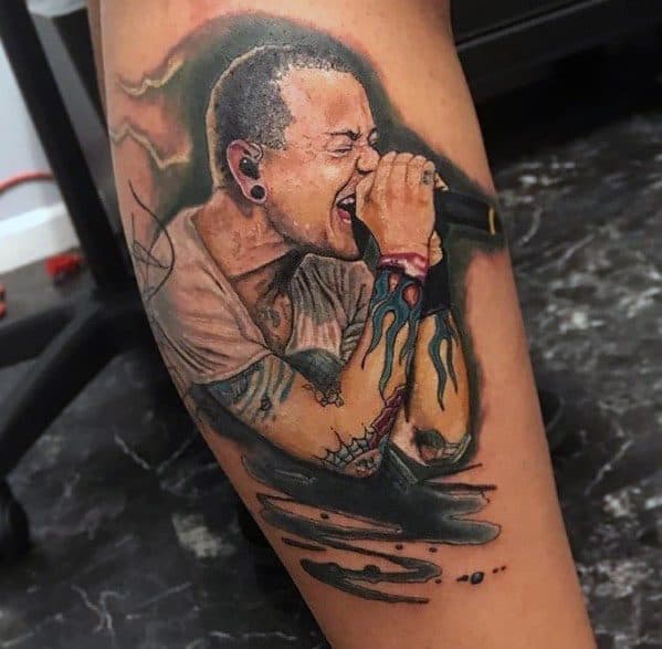 Realistic color tattoo of Chester Bennington singing, featuring his iconic flame wrist tattoo and dynamic shading on the leg.