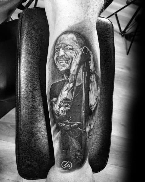 Realistic black and gray tattoo of Chester Bennington smiling on stage, featuring detailed shading and the Linkin Park logo at the bottom.