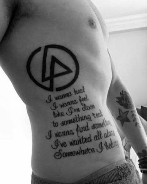 Black ink Linkin Park logo tattoo on the ribs, accompanied by lyrics from 'Somewhere I Belong' in elegant script font.