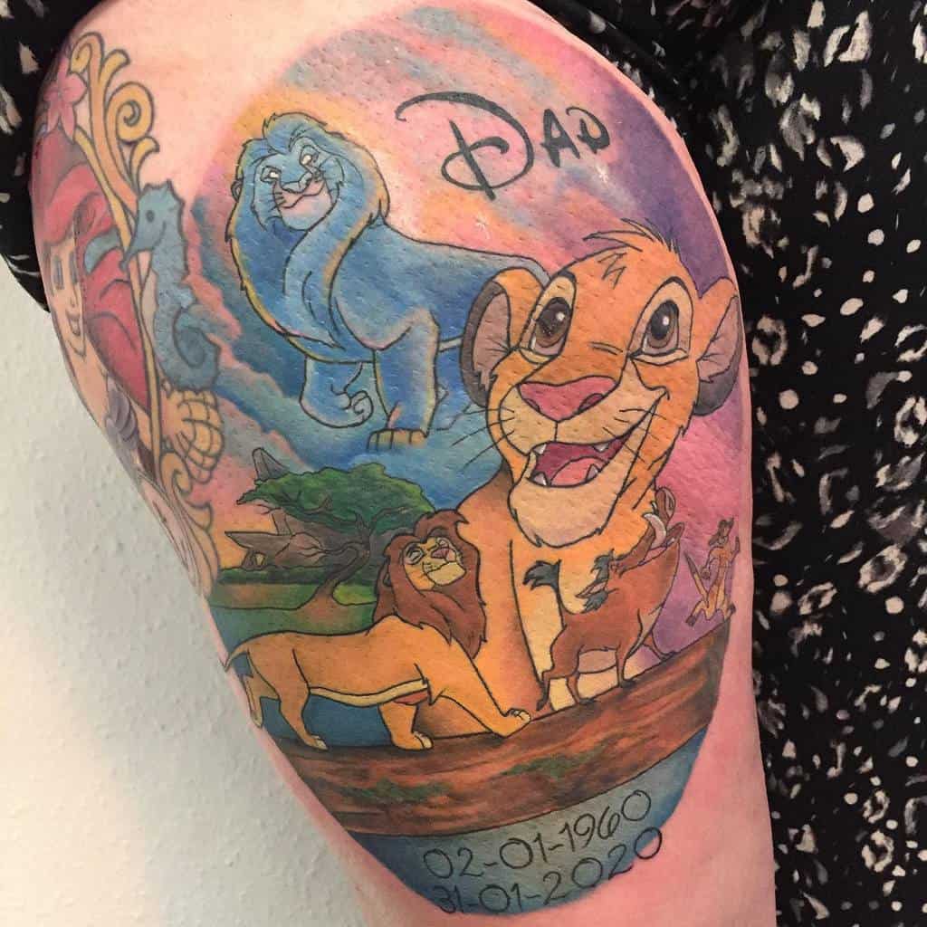 Colorful memorial tattoo featuring Simba, Mufasa, and a blue spirit lion, along with other animals from the savanna, with 'Dad' inscribed above, and the dates 02-01-1960 to 31-01-2020 below