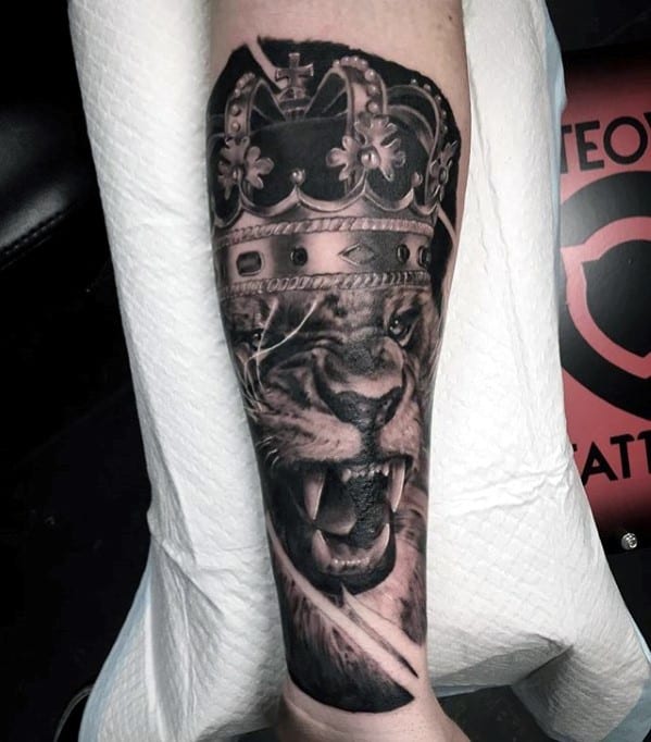A tattoo of a roaring lion wearing a crown on a person's forearm
