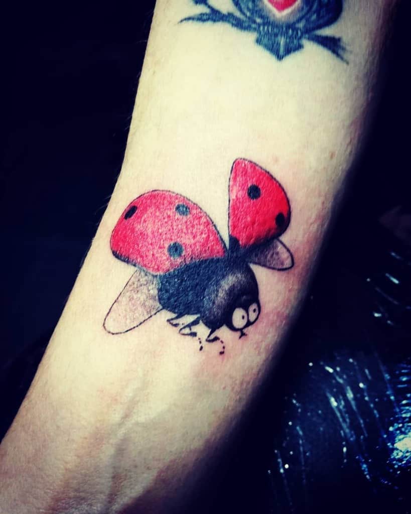 Playful ladybug tattoo with cartoon-style wide eyes, vibrant red wings, and fine shading, creating a fun and whimsical design.