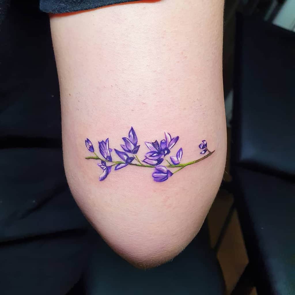 Minimalist tattoo featuring a delicate branch of lilac flowers in vibrant purple hues, placed on the inner arm