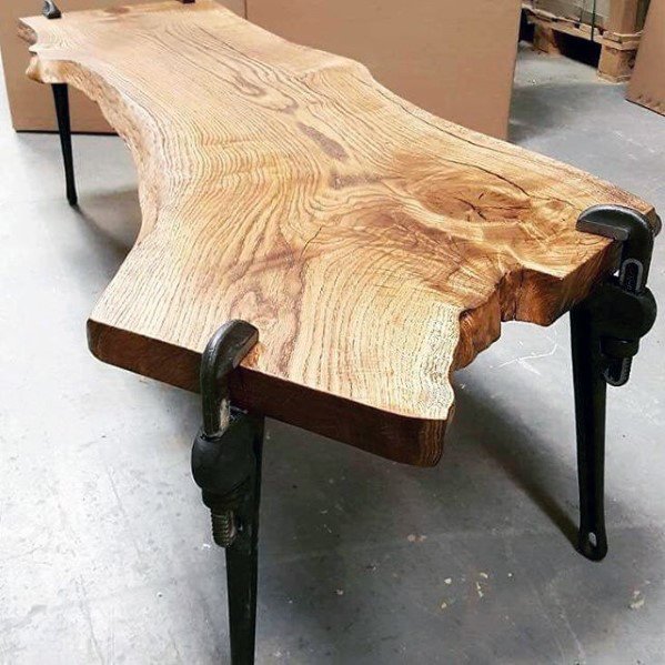 Wooden table with natural edges and pipe wrench legs on a gray floor