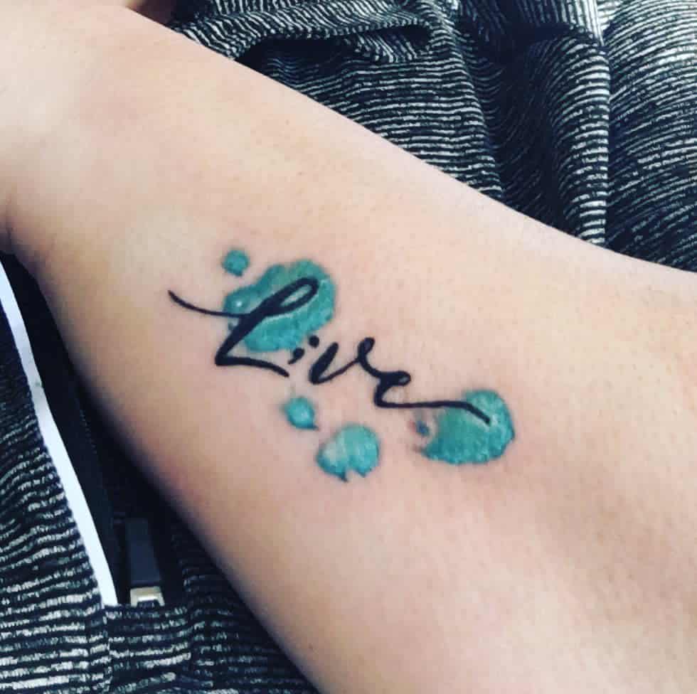 This tattoo features the word "Live" with a vibrant ink splash design, creating a lively and artistic expression of living in the moment.