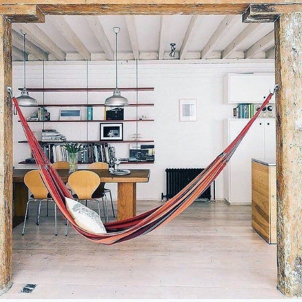 Red hammock in a bright open-plan living space with wooden beams and modern decor.