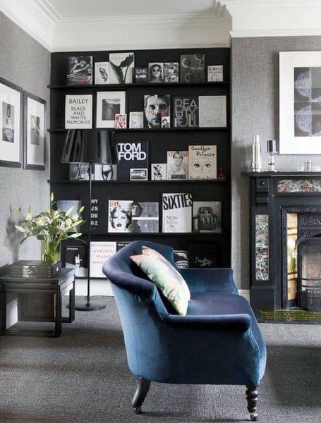 Stylish room with a blue chaise, black bookcase filled with fashion-themed books, and a decorative fireplace