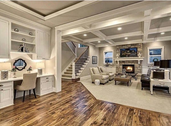 Spacious living room with a coffered ceiling, hardwood floor, stone fireplace, and a built-in desk near stairs