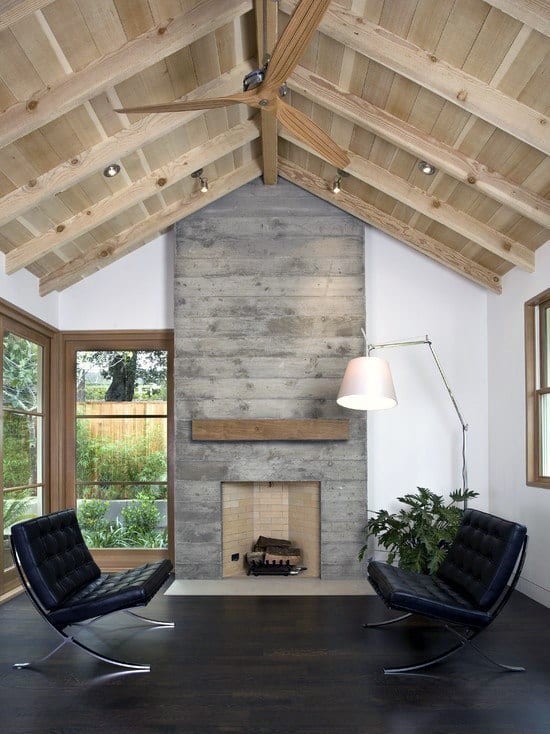 Modern concrete fireplace with a wooden mantle in a vaulted-ceiling living room.