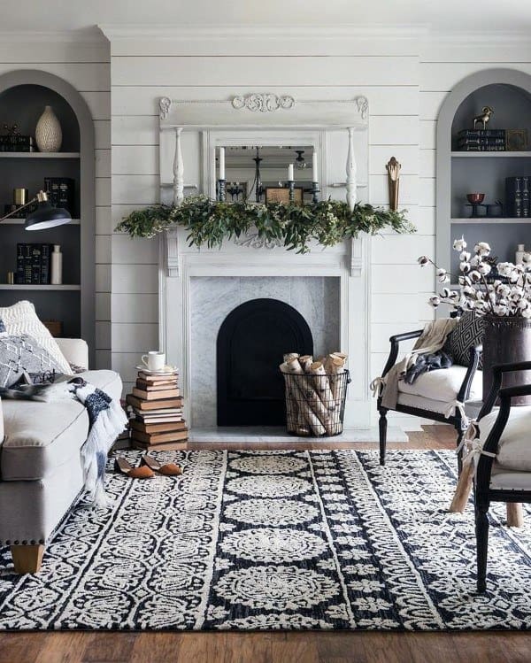 Cozy living room with a white shiplap fireplace, greenery mantel decor, and patterned rug.