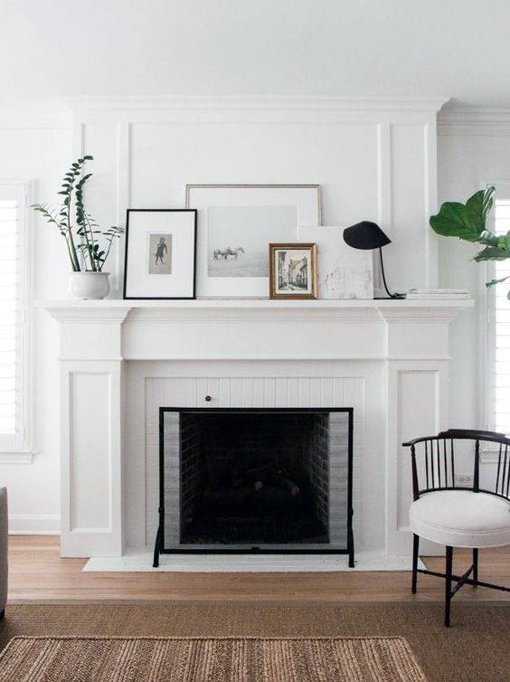 Traditional white fireplace with a decorative mantel displaying framed art and potted plants.