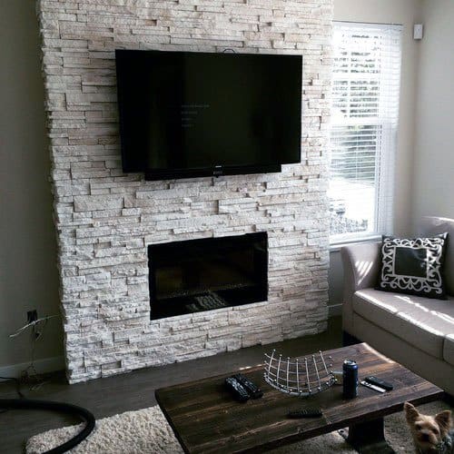 Minimalist living room with a white stacked stone fireplace, mounted TV, and rustic wooden coffee table