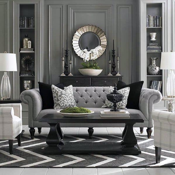 Elegant living room with gray built-in bookcases, tufted sofa, chevron rug, and decorative mirror centerpiece