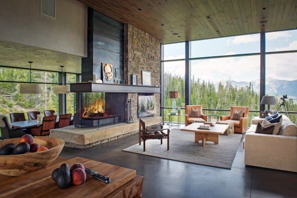 Modern living room with large windows, stone fireplace, and concrete floor, cozy seating and fruit bowl on the table