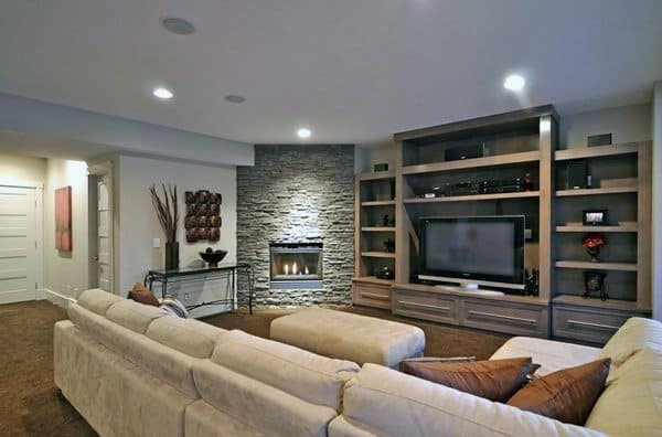 Contemporary living room with gray stone corner fireplace, beige sectional sofa, and built-in shelves.