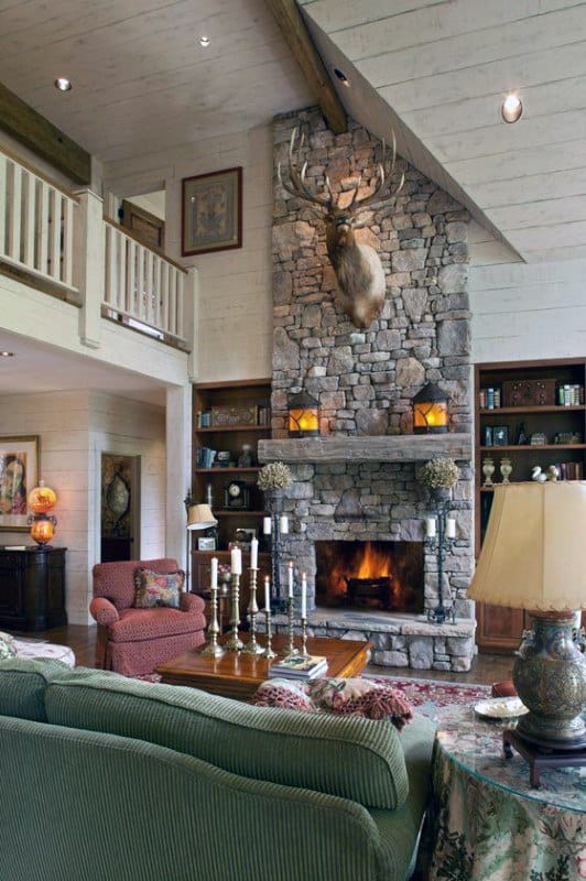 Cozy living room with tall stone fireplace, mounted deer head, and rustic wooden mantel.