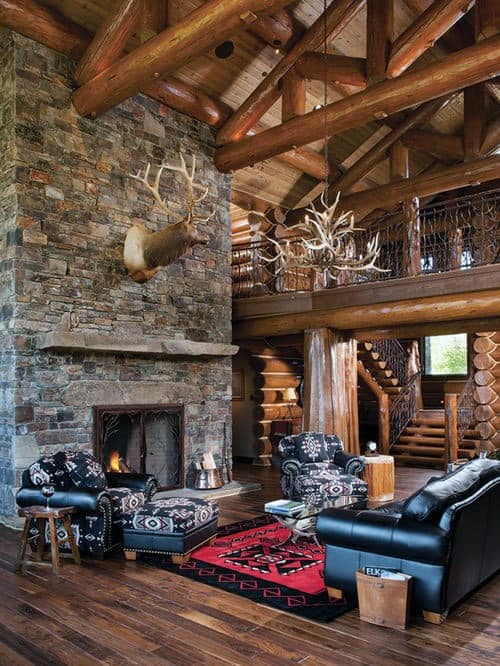 Log cabin living room with stone fireplace, antler chandelier, and rustic wood beam architecture.