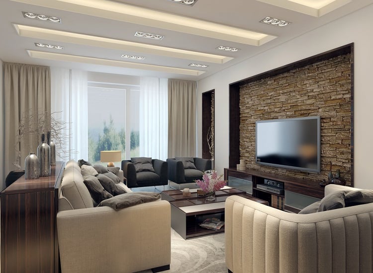 A modern living room featuring a floating ceiling with recessed lighting, stylish furniture, a stone accent wall, and large windows that let in natural light, creating a bright and sophisticated space