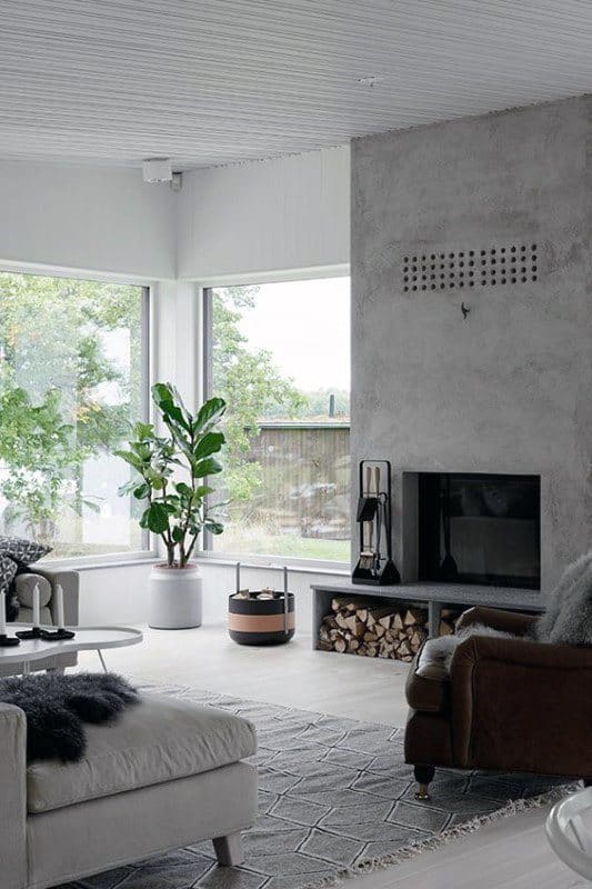 Minimalist concrete fireplace in a bright living room with large windows and cozy modern decor.