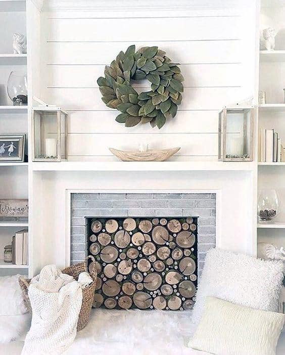 White shiplap fireplace with stacked log decor, a green wreath, and lantern accents on the mantel.