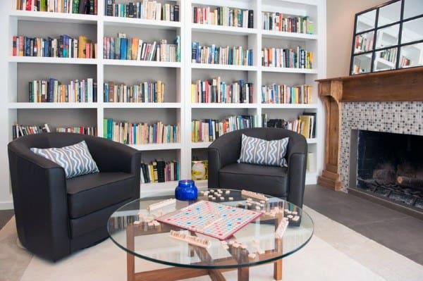 Cozy library with bookshelves, two chairs, a fireplace, and a glass table featuring a Scrabble board