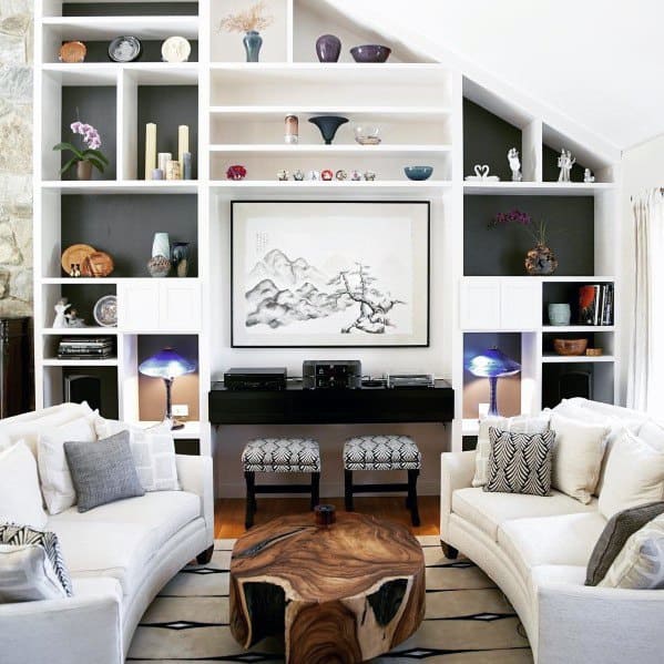 Contemporary living room with white built-in bookcases, artistic decor, curved sofas, and a unique wooden coffee table