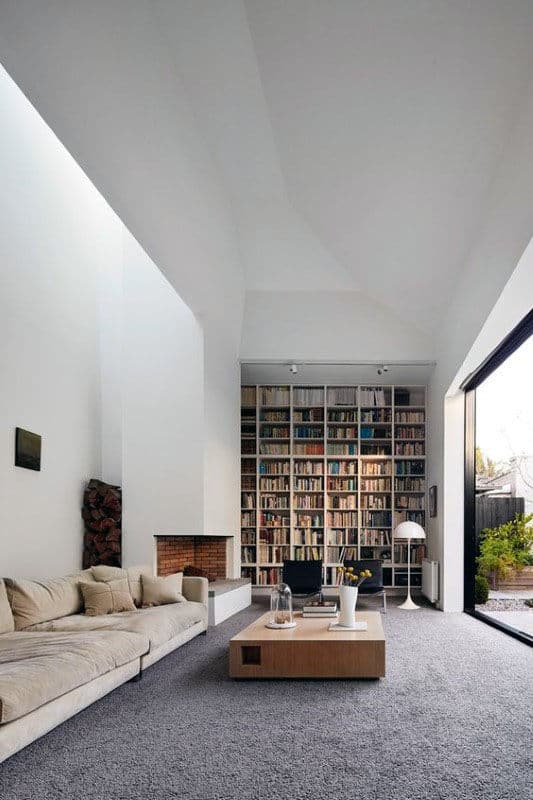 Modern living room with tall library-style bookshelves, beige sofa, and large glass doors opening to a garden