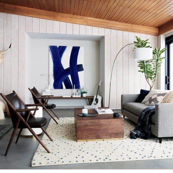 Modern living room with wood ceiling, shiplap walls, leather chairs, gray sofa, and decor accents.