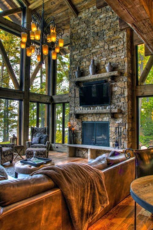 Rustic living room with floor-to-ceiling stone fireplace, leather sofa, and large windows.