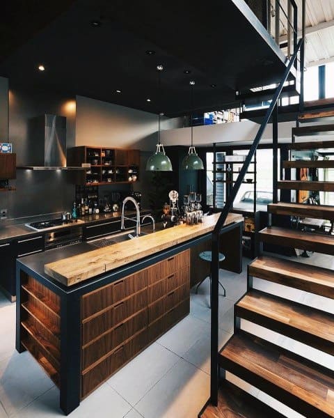 Modern loft kitchen with wooden island, dark accents, and floating staircase design.