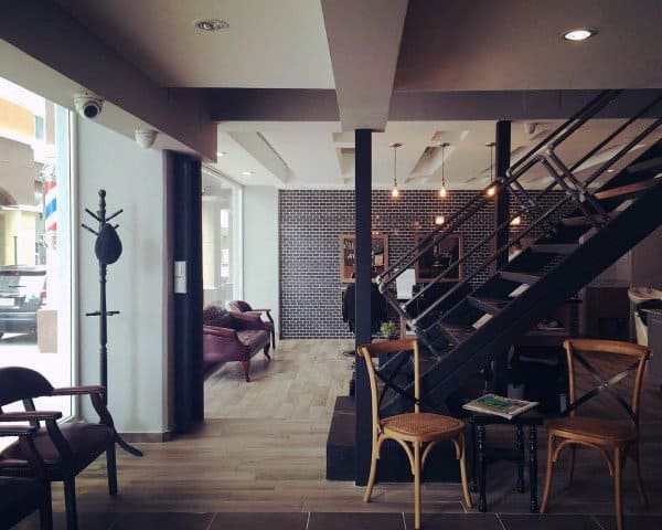 Loft-style barber shop with brick wall, staircase, seating area, and industrial decor.