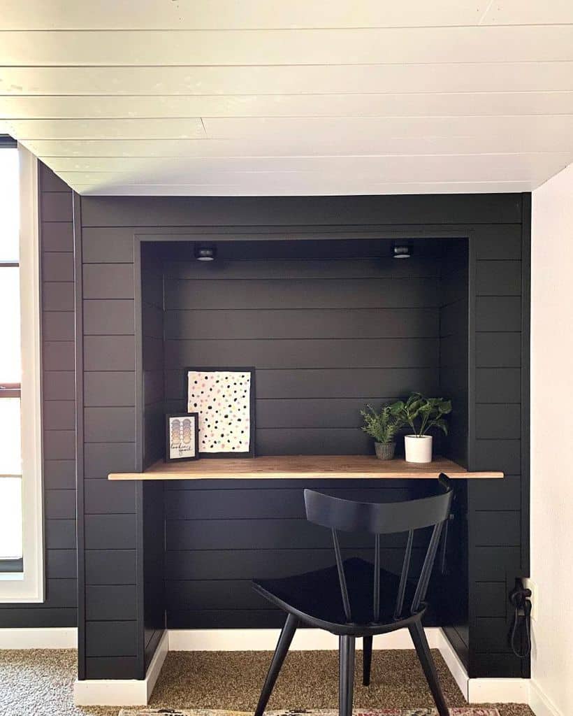 Cozy loft desk nook with black shiplap walls, wood desk, and black chair.