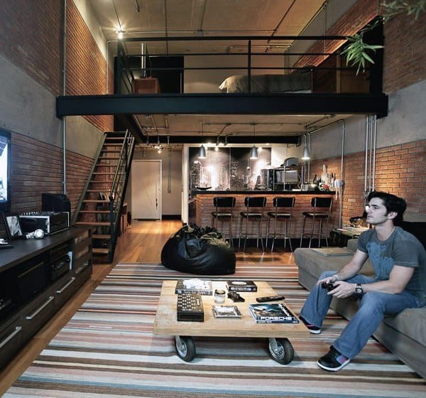 Industrial loft with exposed brick walls, mezzanine bedroom, and cozy living area with striped rug.