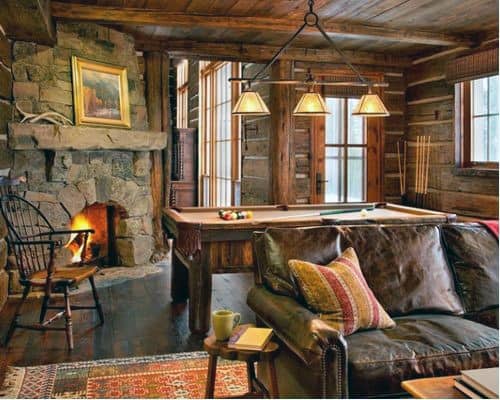 Rustic log cabin with stone fireplace, leather sofa, pool table, and warm pendant lighting.