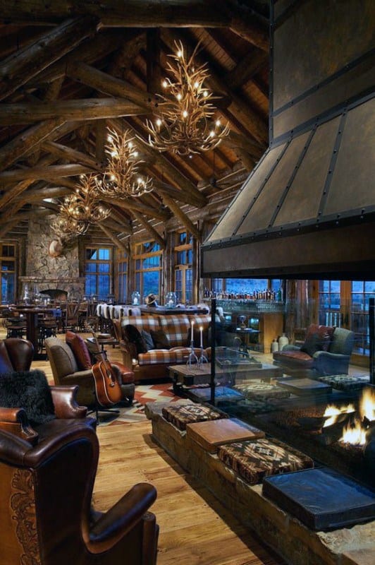Rustic log cabin great room with vaulted ceiling, antler chandeliers, and a modern glass fireplace.