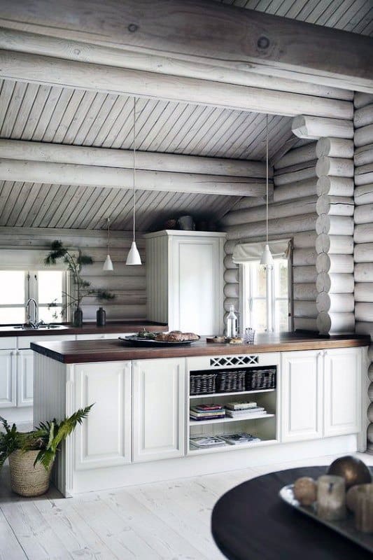 Bright and modern log cabin kitchen featuring white cabinetry, dark wood countertops, and soft pendant lighting.