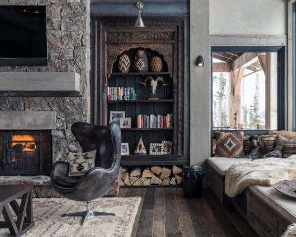 Rustic log cabin with a stone fireplace, built-in bookshelf, and cozy seating nook.